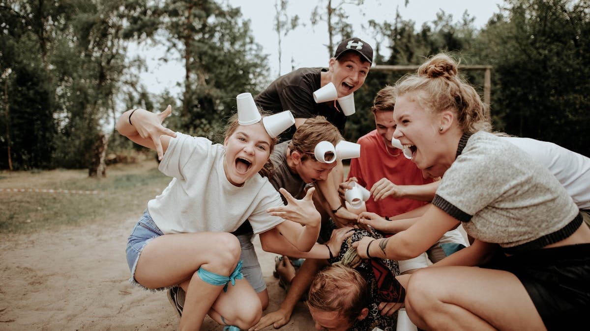 Energetic group of teenagers playing outdoors, with laughter and cups in a pile.